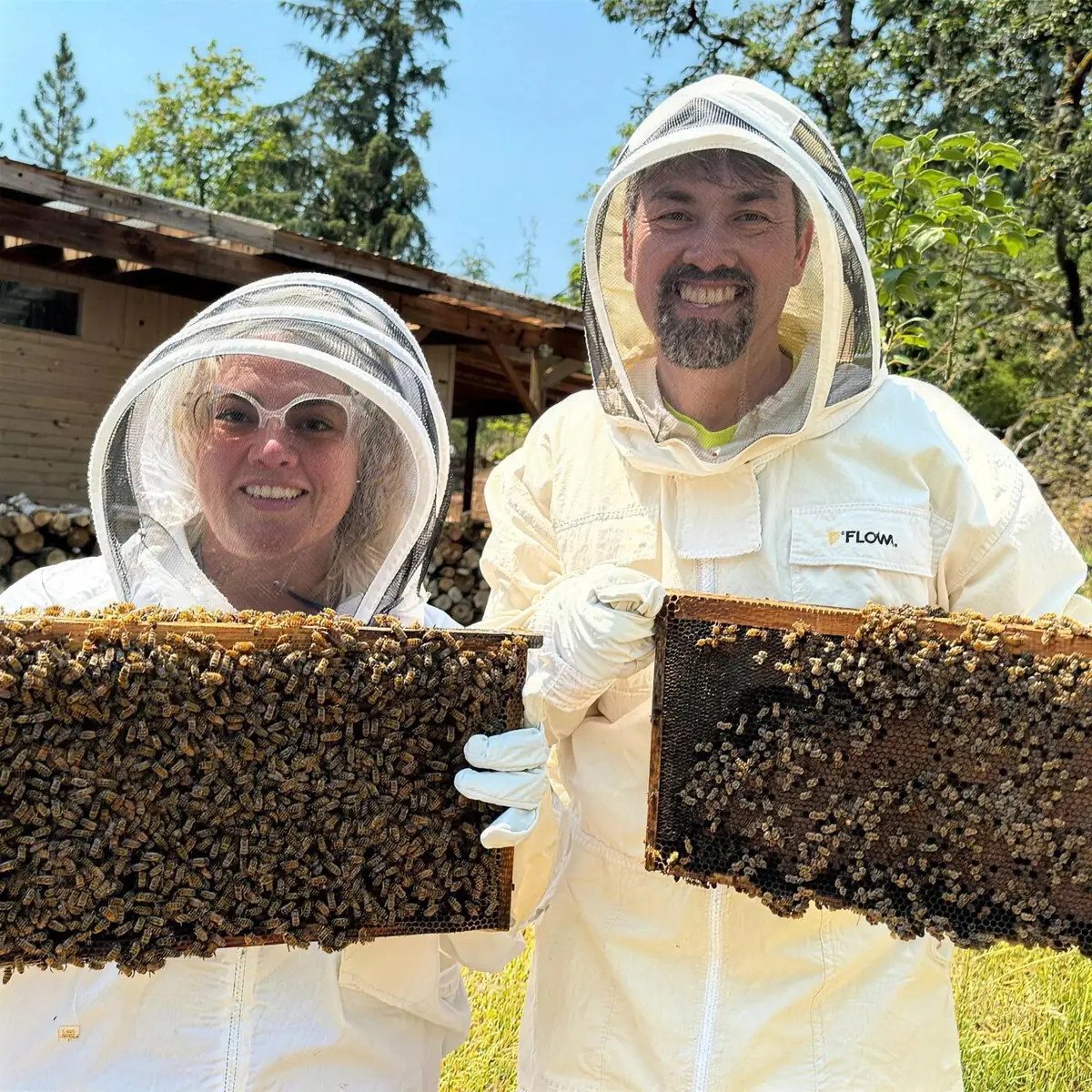 Kathryn and Geoff Belleville in bee suits and veils, each holding up a frame covered in bees